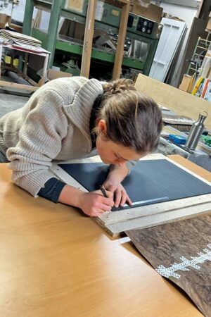 Johanna Thielges arbeitet konzentriert an einem Möbelstück. Das ausgewählte Furnierblatt ist bereits für die Weiterverarbeitung vorbereitet. Foto: Kevin Thielges